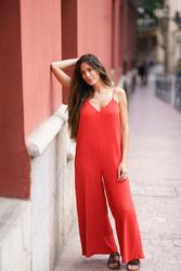 An Elegant Woman Dressed in a Stunning Red Jumpsuit Posing Gracefully Against a City Wall