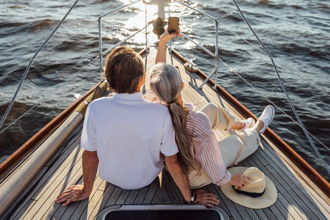 Two older adults sitting together on a yacht bow and taking selfie