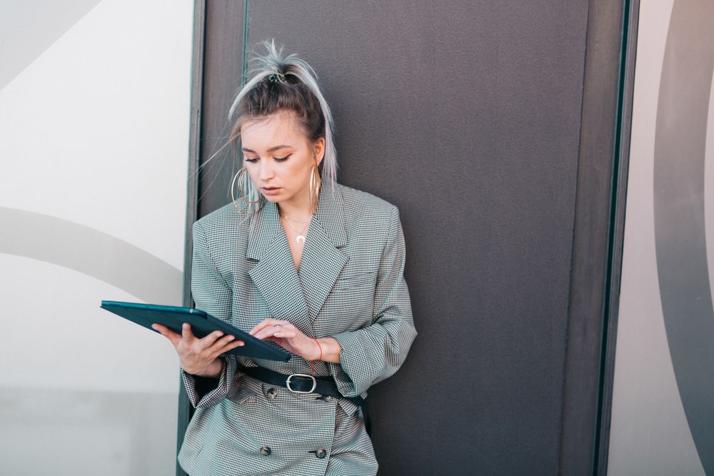 Stylish businesswoman with laptop leaning on wall