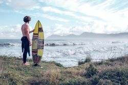 Male surfer in wetsuit and with board admiring waves on seashore