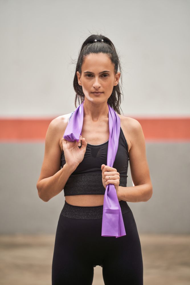 Unemotional sportswoman standing in gym with elastic band