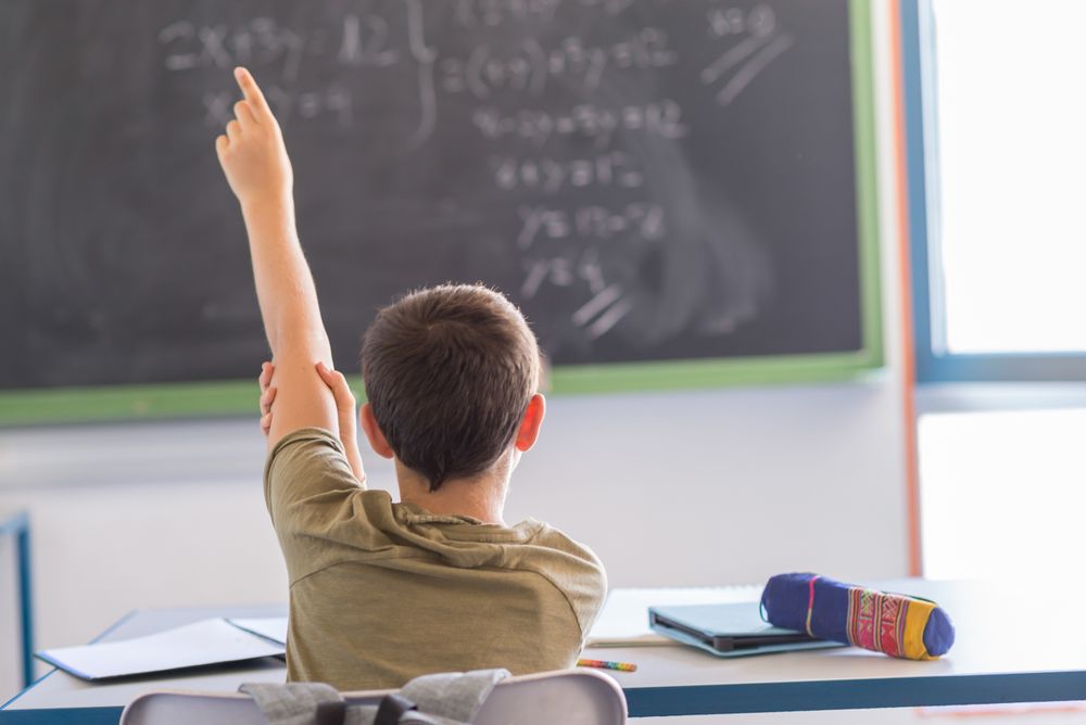 Back of teenager holding arm up to ask question in class