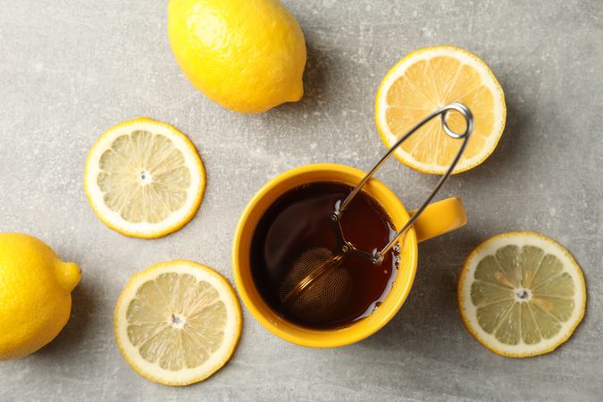 Cup of tea and lemons on grey background, top view