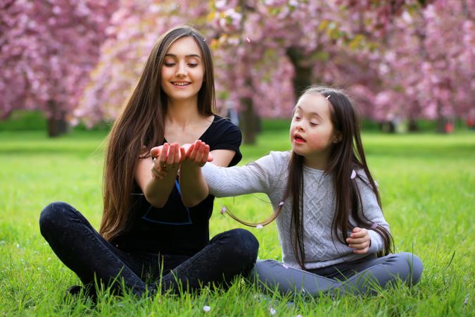 Sisters playing at a park catching flower petals fall from trees