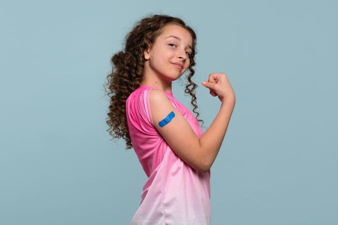 Girl flexing arm with blue bandage after vaccination