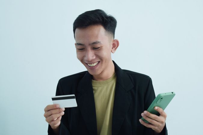 Happy Asian businessman in suit holding blank credit card and smartphone