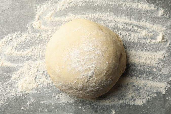 Dough ball and flour on gray background