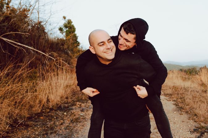 Smiling man holding on back cheerful guy on road on hill
