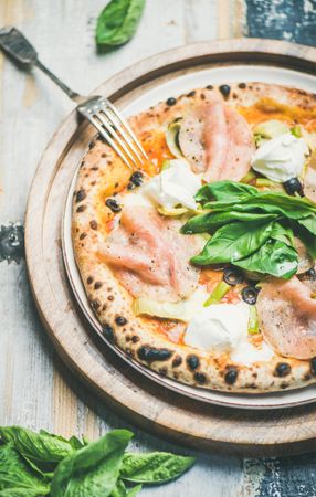 Freshly made wood fire oven pizza with spinach, ham and olives, close up, vertical composition