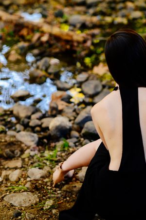 Cropped back view of woman model sitting by a creek in the woods