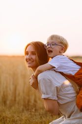 Cheerful mom giving piggyback ride to cute son on wheat field