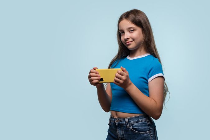 Girl confidently holding smartphone, showing playful smile.
