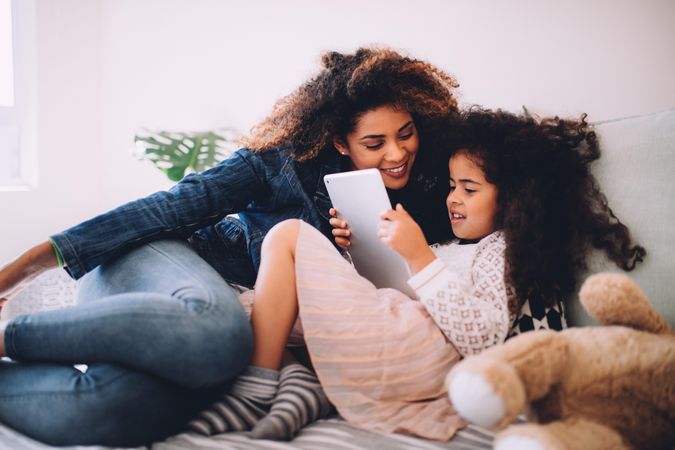 Mother and daughter lying on a bed reading on a tablet