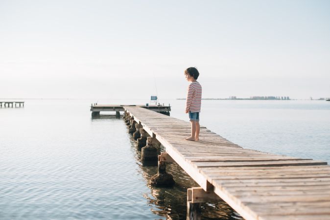 Lonely kid on pier in sunshine
