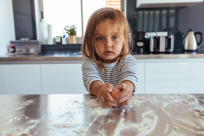 Little girl breaks an egg with flour on the kitchen counter