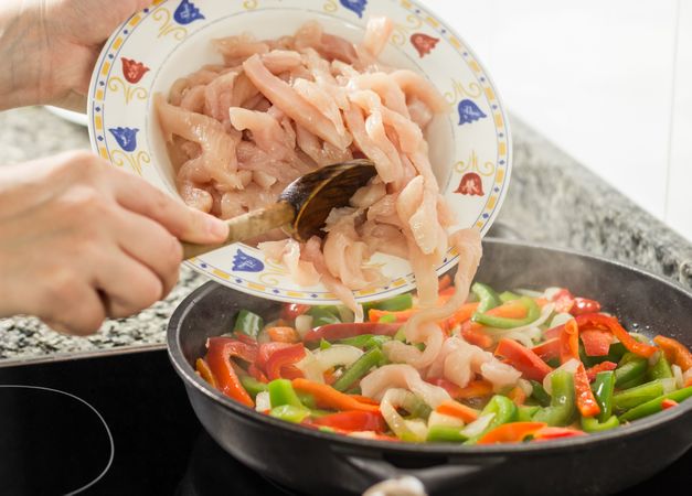 Closeup of female cooking vegetables and chicken in a pan