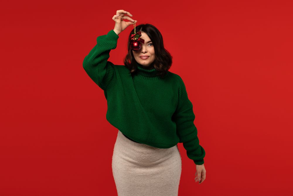 Woman posing with red Christmas ornament in front of eye.
