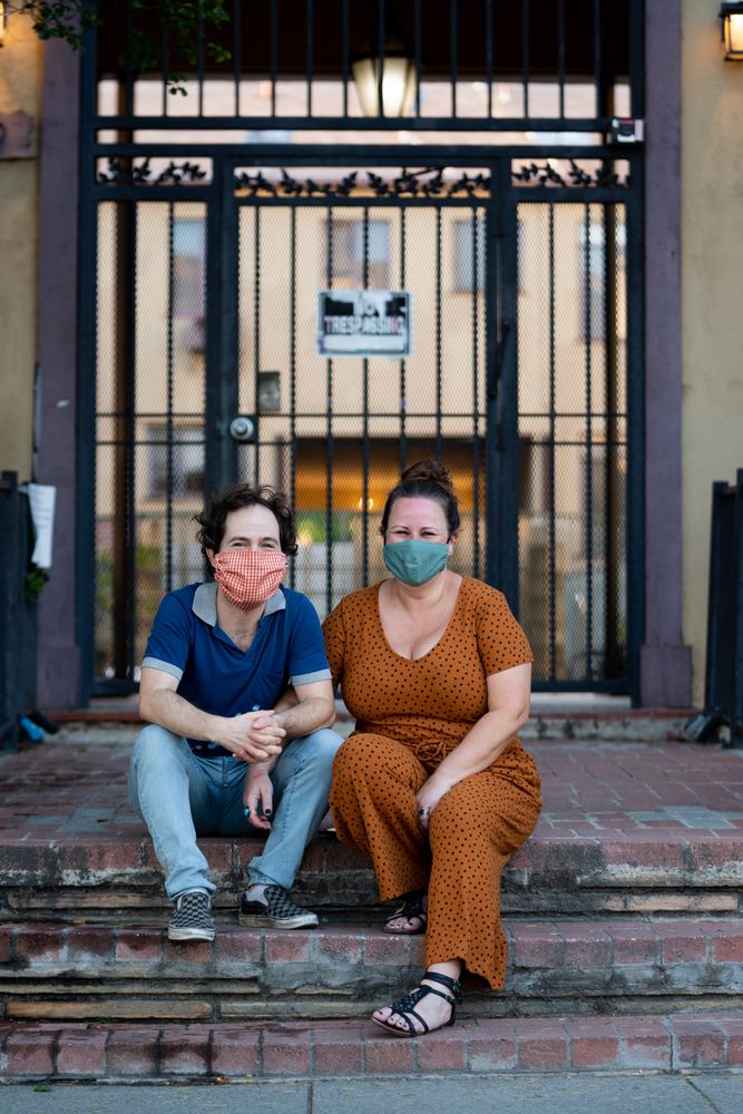 Portrait of loving couple sitting on stoop in front of apartment building with masks