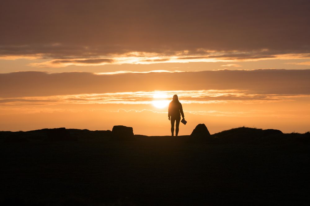 Woman with book standing at sunset