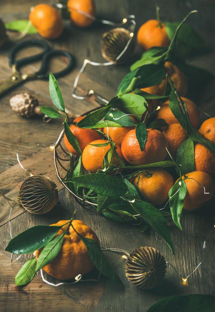 Freshly picked tangerines in wire bowl, with leaves on wooden table, with Christmas decorations