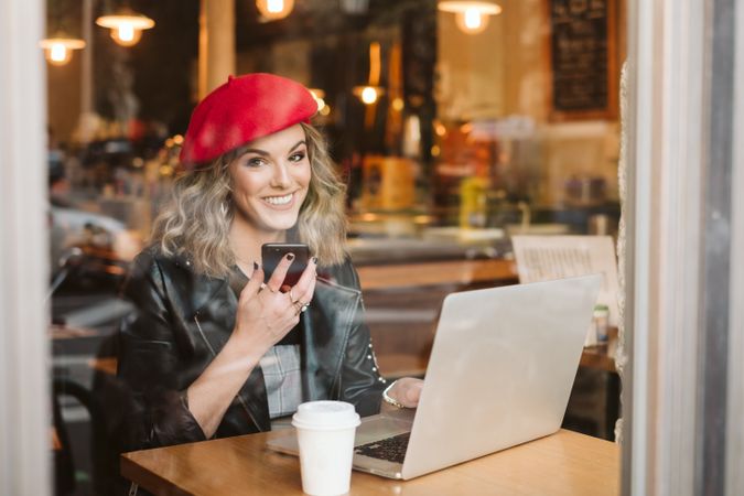 Woman with laptop using smartphone in cafe