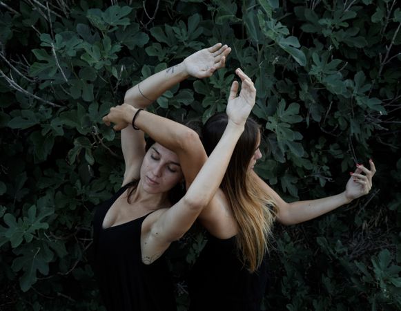 Young women posing near green bush