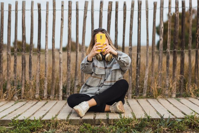 Young woman taking selfie on smartphone witting on wooden path