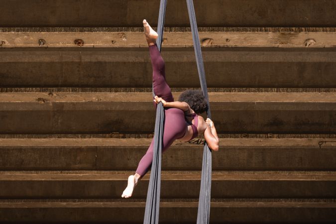 Slim woman doing yoga with aerial silks in city