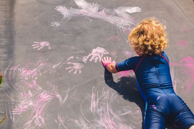 Child printing colors with hands on concrete surface