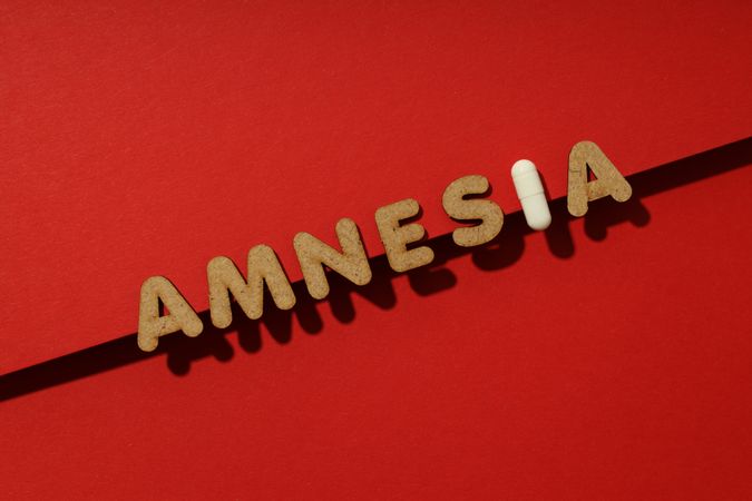 Cork letters of the word “Amnesia” with pill on red background