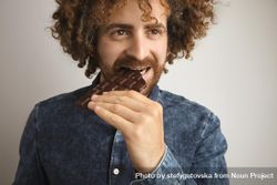 Man with curly hair eating chocolate bar bYm2db