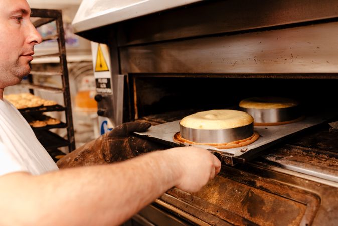 Male baker putting cakes into oven