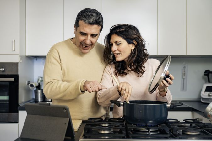 Authentic couple cooking together using online recipe on tablet in modern kitchen
