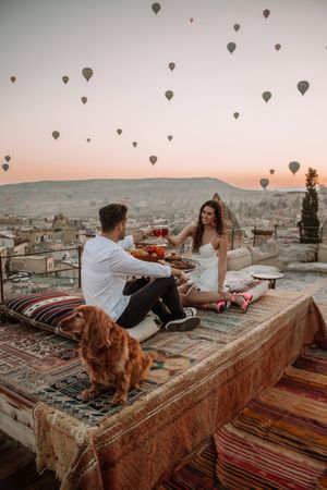Man and woman raising toast on rooftop with hot air balloons in sky