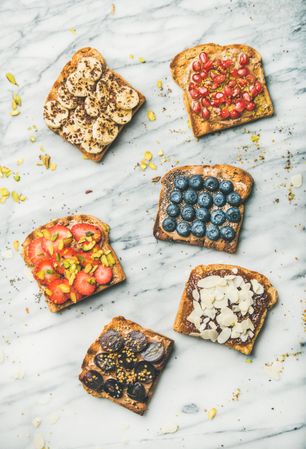 Slices of toasts with different fresh fruit toppings on marble counter