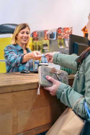 Smiling woman shop assistant taking credit card of client to charge purchase. Local commerce concept