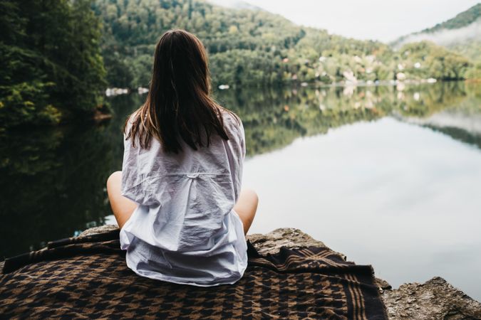 Woman sitting on blanket near lake and mountains