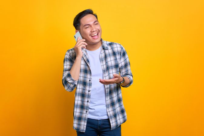 Happy Asian male talking on phone in studio shoot with hand gesture