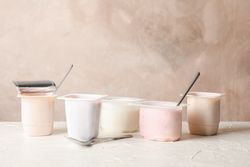 Composition with plastic cups with yogurt on table