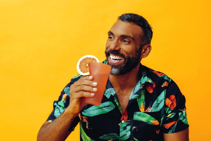 Smiling Black male sitting down with cocktail in yellow room, copy space