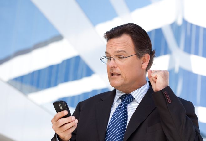 Businessman Looking at Cell Phone Clinches His Fist in Joy