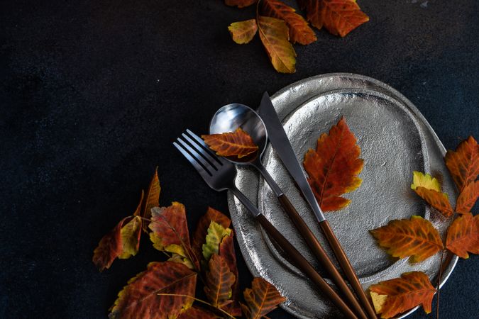 Top view of table settings of shiny ceramic plates with autumn leaves and cutlery