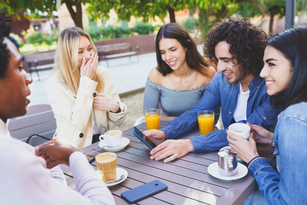 Group of friends having coffee and juice outside and checking phone