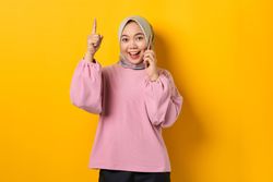 Excited Muslim woman on the phone and pointing upwards with good idea