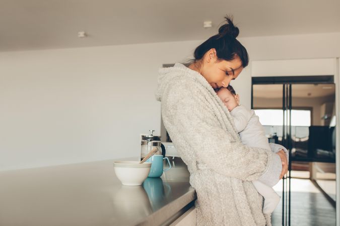 Woman in bathrobe holding her son in kitchen at home