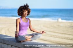 Black woman with afro hairstyle meditating near the ocean 4OaYg0