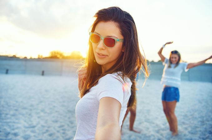 Portrait of brunette woman in sunglasses with her arm out with friends in background on beach
