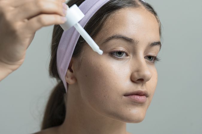Young woman applying face serum or cosmetic essence with a dropper in her beauty routine