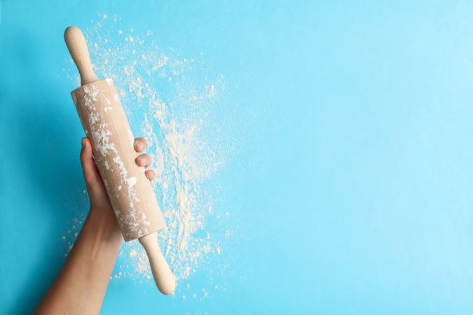 Female hand hold rolling pin on blue background