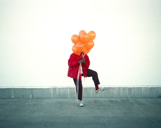 Person in red jacket holding yellow balloons standing against light wall